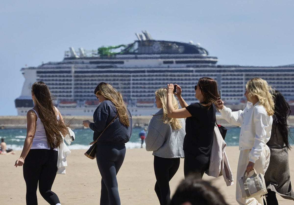 Un grupo de turistas, en la playa, con un crucero de fondo.