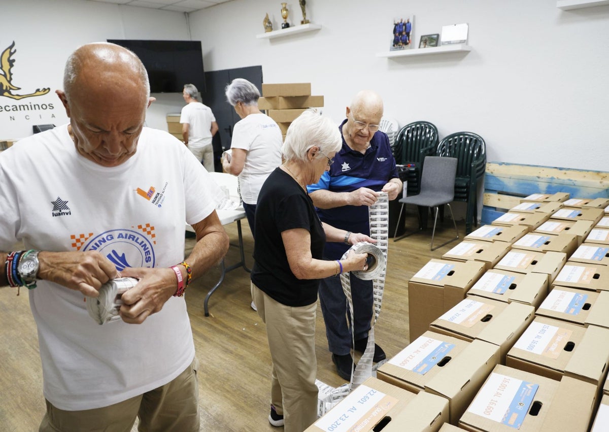 Imagen secundaria 1 - Los voluntarios de la SD Correcaminos preparan los dorsales que lucirán los corredores.