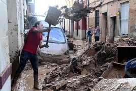 Un hombre saca fango con una pala de su casa en Paiporta.