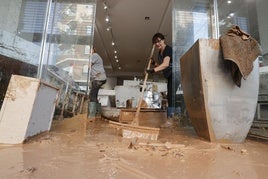 Una mujer extrae agua con lodo de su comercio de Albal.