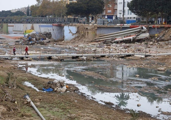 Dos vecinos cruzan por la pasarela provisional construida en el barranco del Poyo a su paso por Picanya, lleno de aguas fecales.