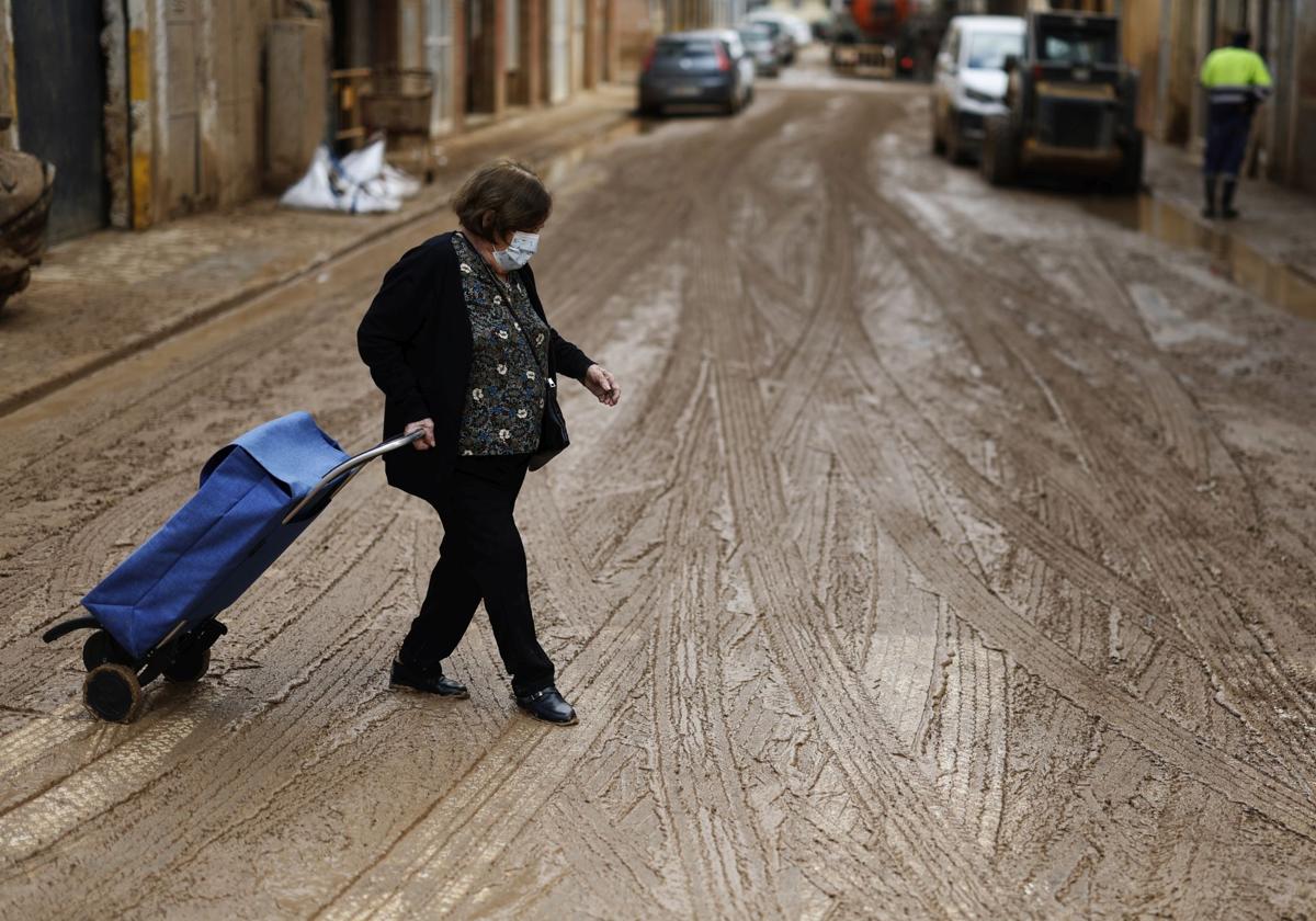 Una mujer intenta no resbalar entre el lodazal que se han vuelto a convertir las calles en Massanassa