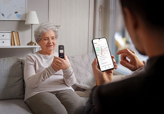 Una señora, con el dispositivo mientras el cuidador accede a la app.