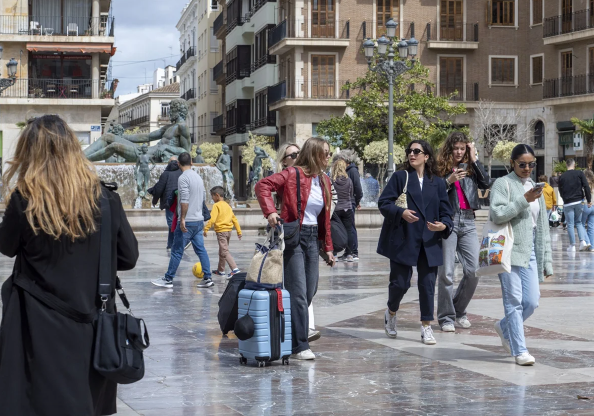 Varias viajeras pasean por la plaza de la Virgen con sus maletas tras llegar a Valencia.