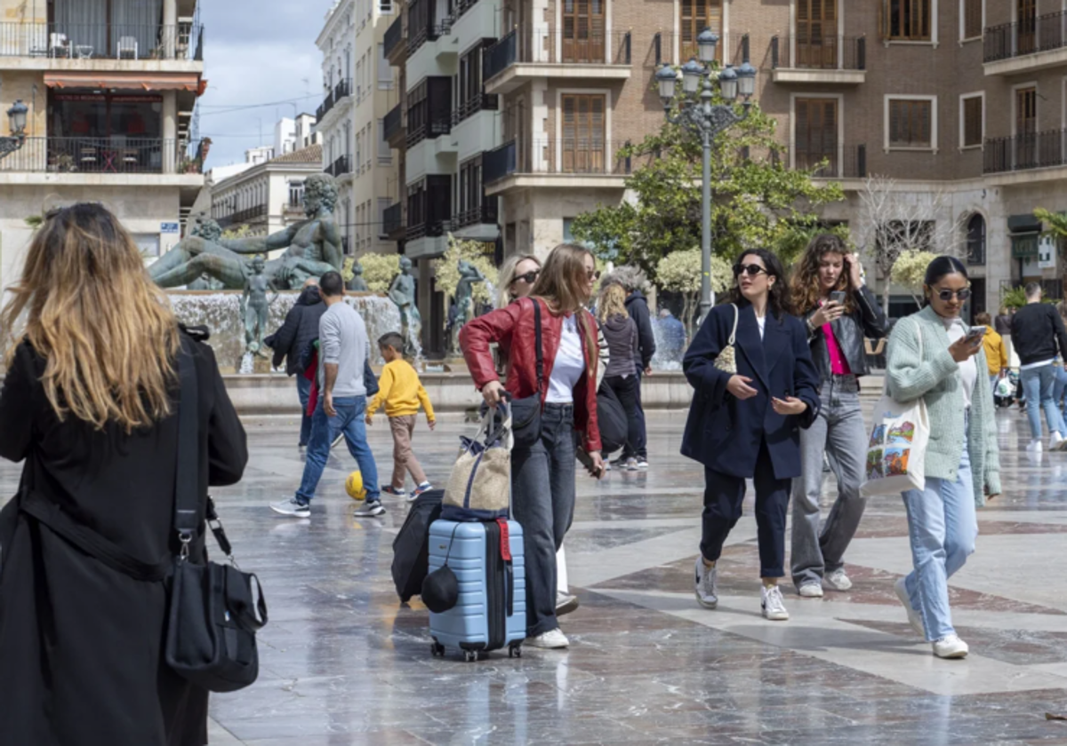 Varias viajeras pasean por la plaza de la Virgen con sus maletas tras llegar a Valencia.