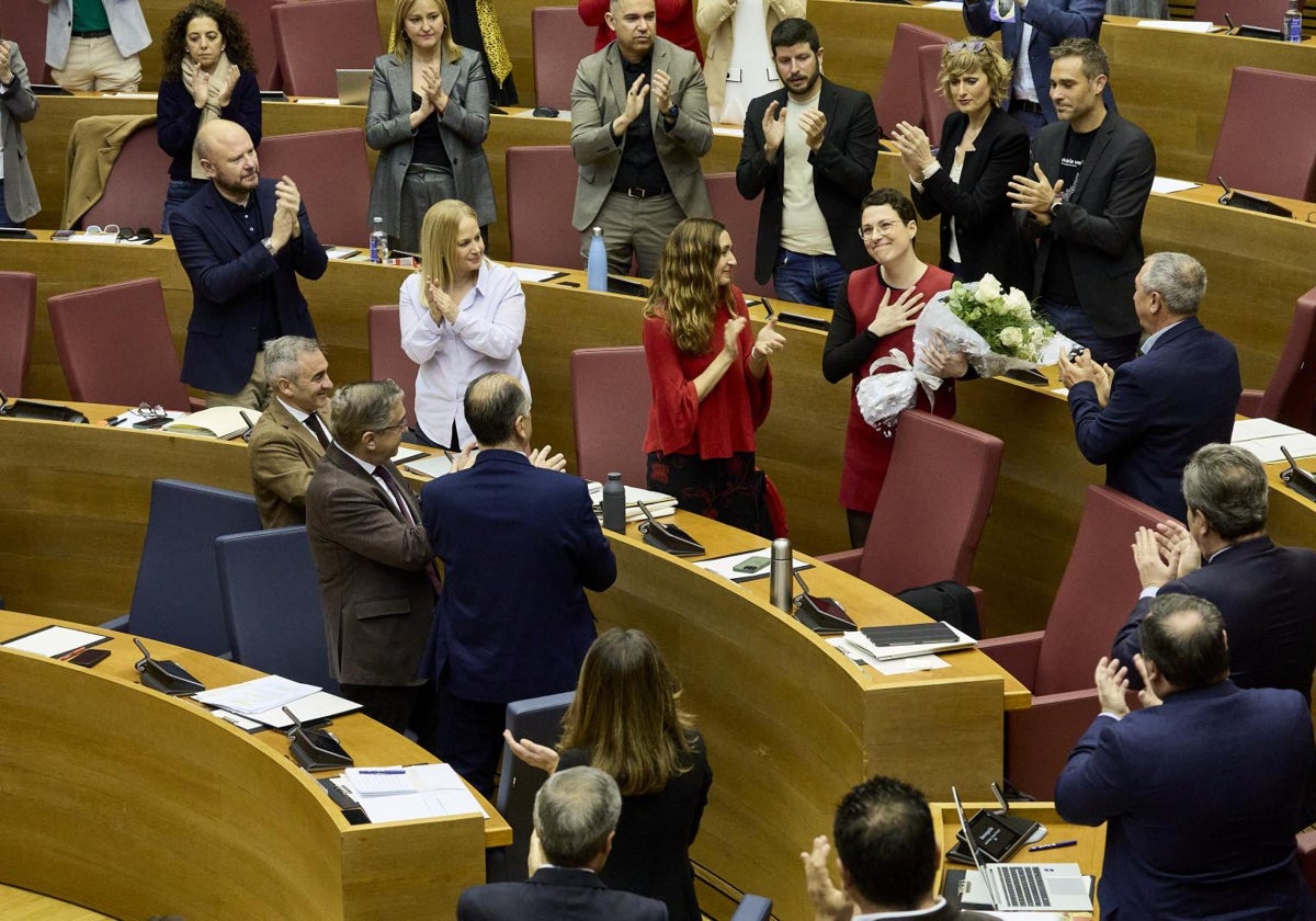 Mas recibe un ramo de flores de sus compañeros de Compromís en Les Corts mientras aplauden en pie los diputados de su grupo, del PSPV, del PP, de Vox y los miembros del Consell.