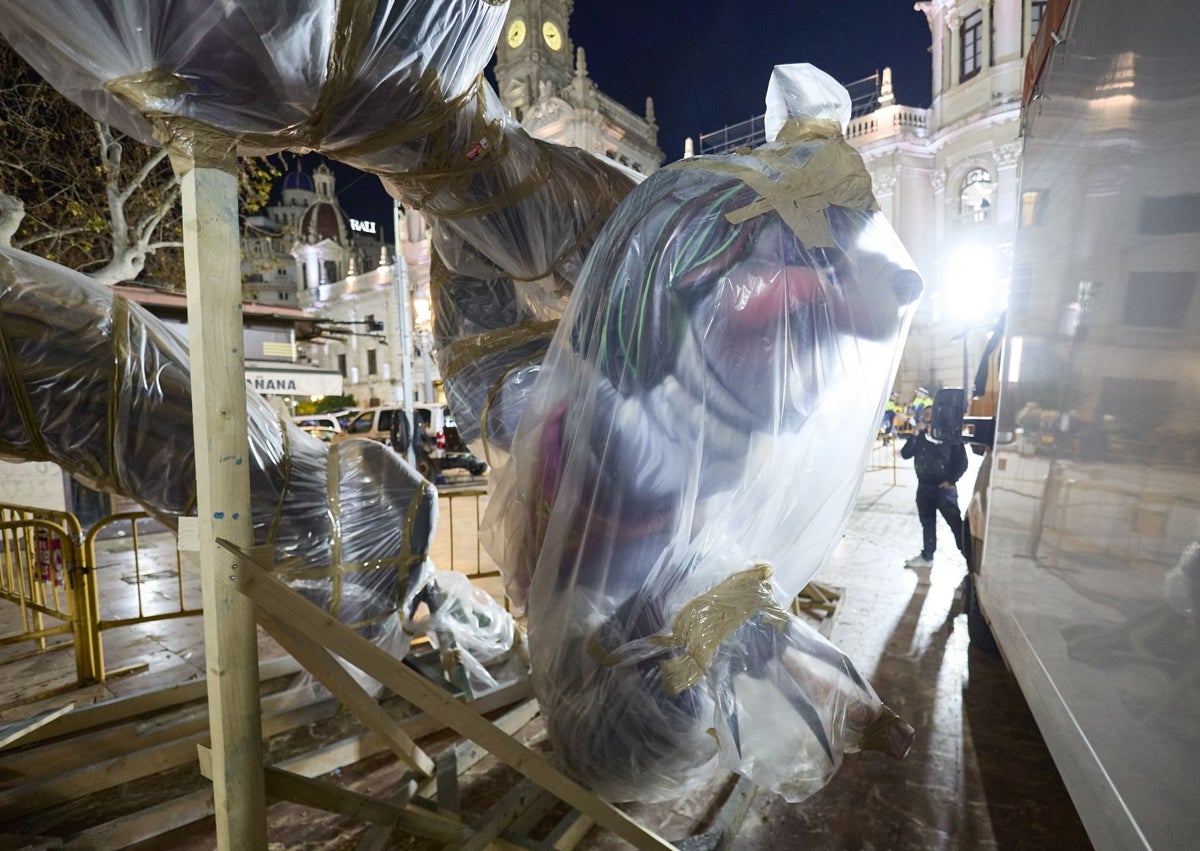 Imagen secundaria 1 - Escena de la fallera a punto de resbalarse y figura del Perezoso que tenía que haber salido de colofón en la Cabalgata del Ninot la semana pasada, ya tapada con plásticos en la plaza.