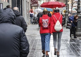 Dos chicas con peinado de falleras pasean bajo la lluvia en Valencia.