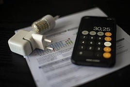 Una factura de la luz junto a una calculadora y un cargador.
