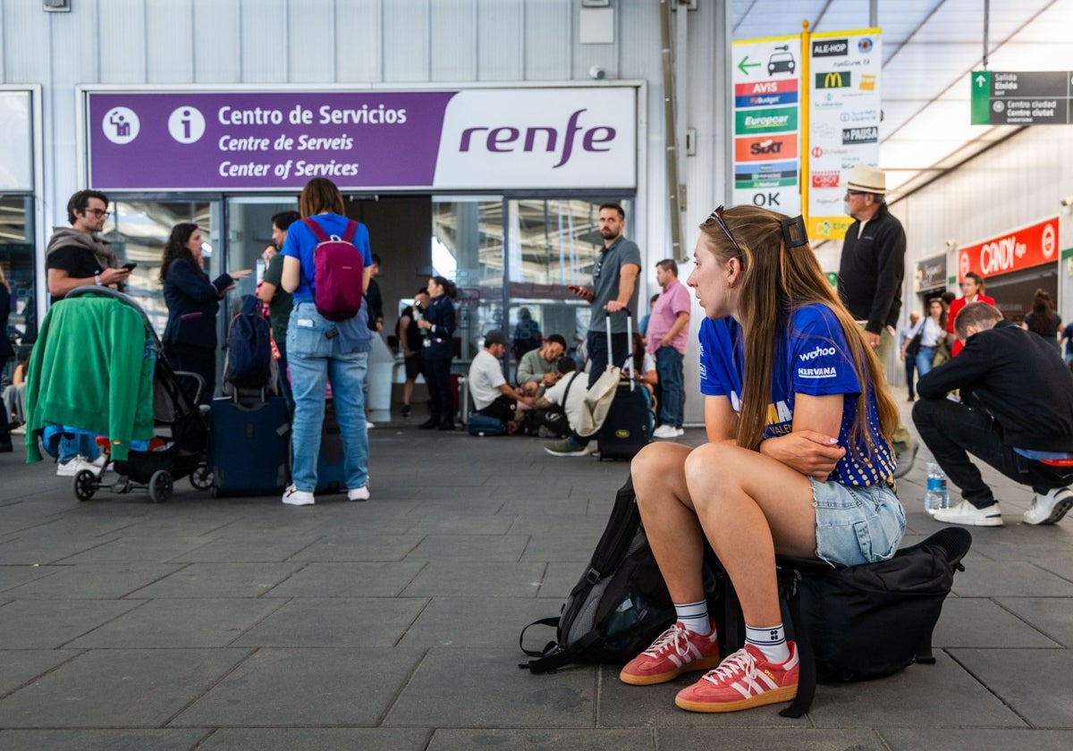 Una usuaria del AVE espera sentada sobre su equipaje en la estación.