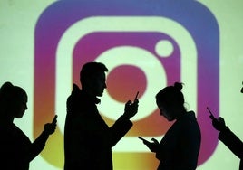 Varias personas usando el móvil delante de una pantalla con el logo de Instagram