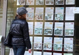 Una mujer mira viviendas en alquiler en el escaparare de una inmobiliaria, imagen de archivo.