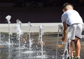 Un niño se refresca en una fuente pública.