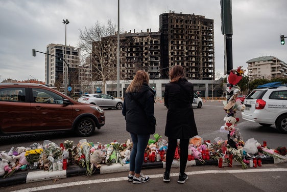 Dos jóvenes, ante el edificio calcinado y las ofrendas florales tras la tragedia.