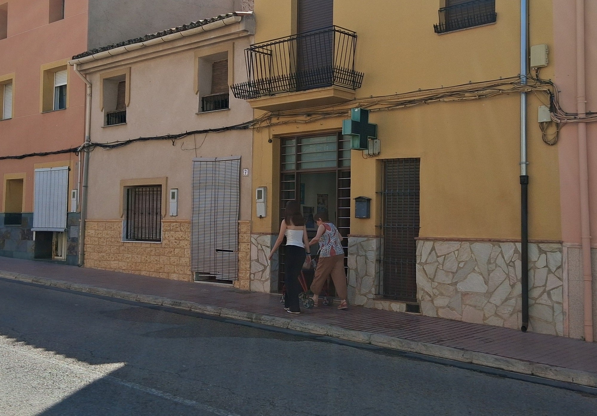 Una persona mayor pasa junto a la farmacia de Cerdà. Abajo, carteles en la puerta de la farmacia de Vallés informando a los pacientes de la situación.