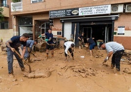 Varias personas limpian una calle en Catarroja, tras la dana.
