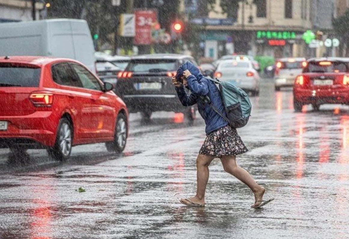 Una chica se intenta refugiar de la lluvia.