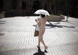 Una mujer se proteje del sol con una sombrilla.