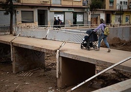 Una mujer cruza un puente, con un carrito de bebé, en Aldaia tras la dana.