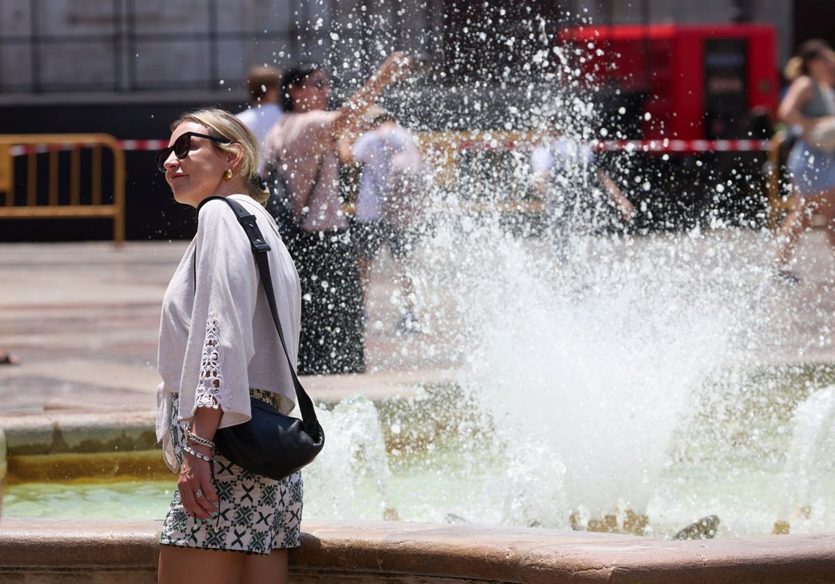 Una mujer trata de mitigar el calor junto a un chorro de agua.