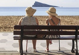 Dos turistas sentadas en un banco, junto al litoral de Benidorm.