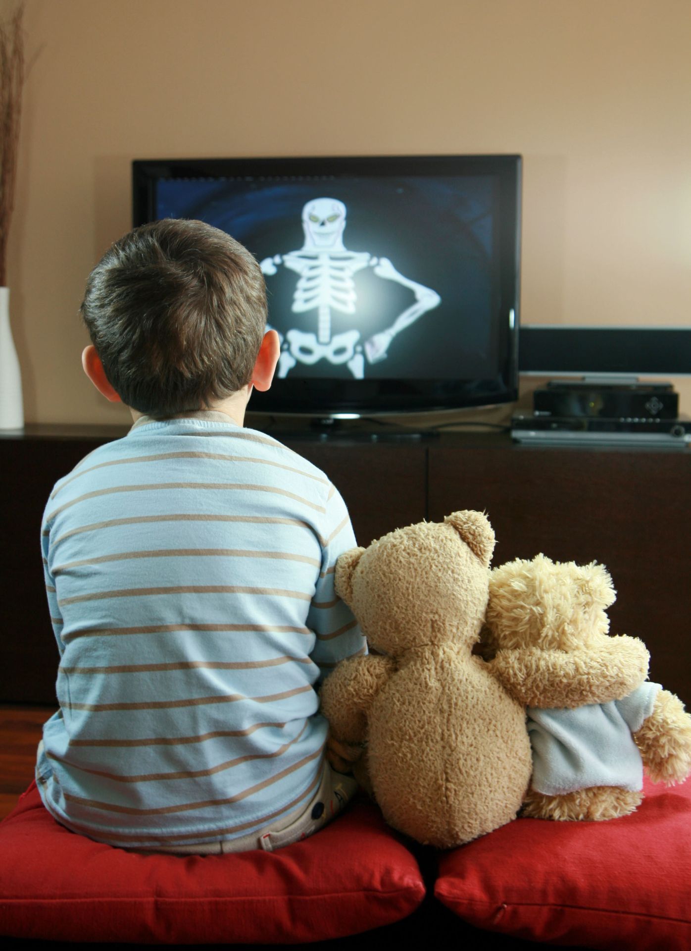 Niño ve la televisión junto a dos muñecos de peluche