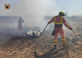 Dos bomberos trabajan para apagar el fuego que ha calcinado la avioneta.