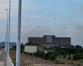 El humo del incendio tras el hospital Lluís Alcanyís y uno de los helicópteros que trabajan en la zona.