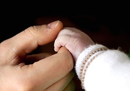 Una mano adulta sosteniendo la mano de una bebé