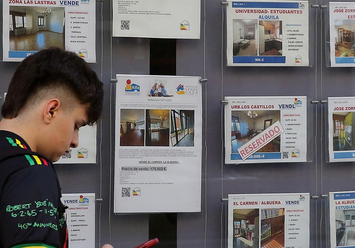 Un joven pasa por delante de un escaparate con anuncios de una inmobiliaria.