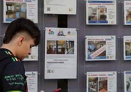 Un joven pasa por delante de un escaparate con anuncios de una inmobiliaria.