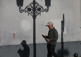 Hombre jubilado pasea por la calle con periódico en mano.