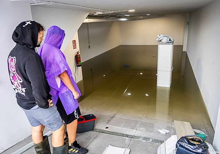 Dos vecinos de los adosados inundados en Alcàsser observan como después de vaciar el garaje se les ha vuelto a llenar de agua.