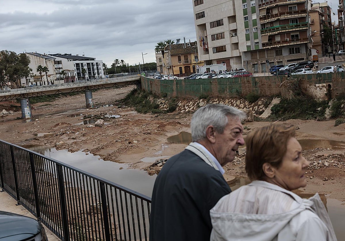Dos personas observan el barranco de Chiva a su paso por Paiporta, este lunes.