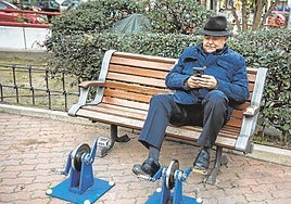 Un jubilado revisa su teléfono sentado en un parque, imagen de archivo.