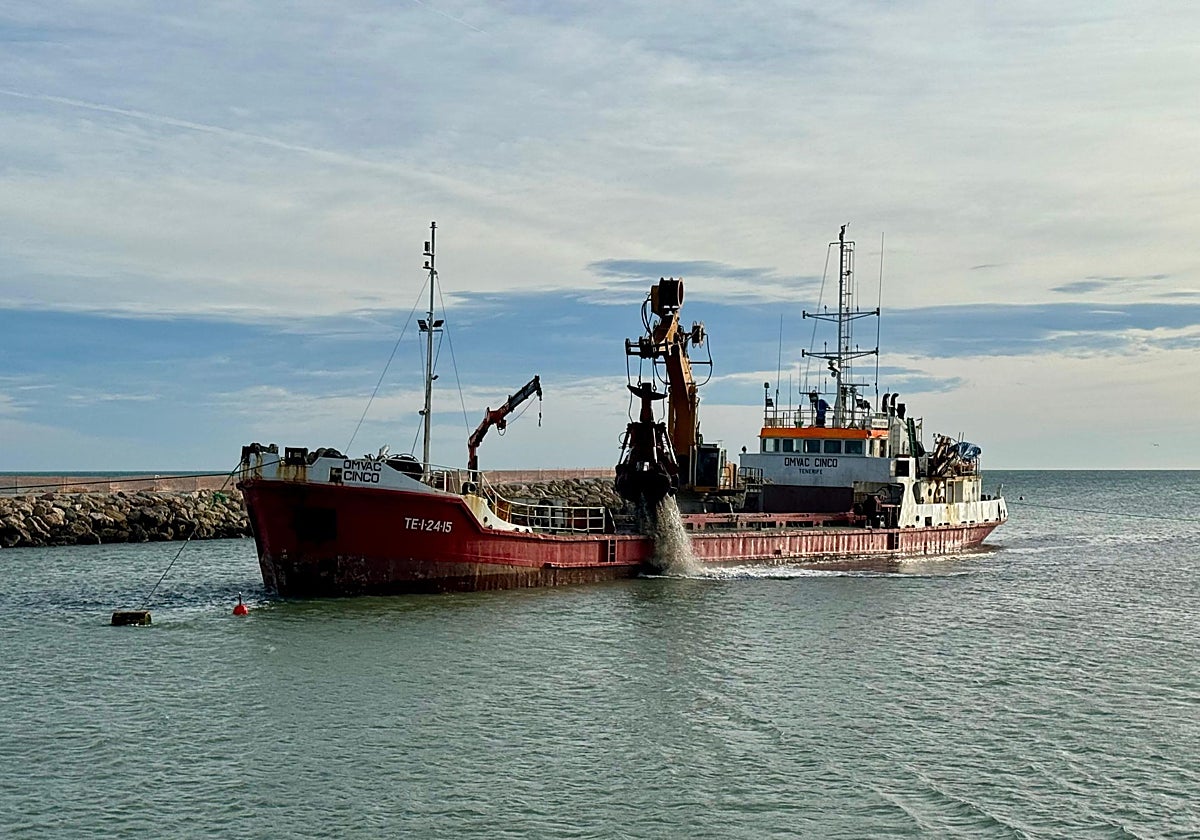 Un barco draga la arena del puerto de Cullera.
