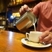 Un camarero pone leche en un café.