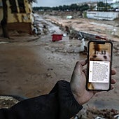 Un hombre sostiene un móvil en medio de una Catarroja embarrada con el Es-Alert que mandó Emergencias a las 20.11 horas del 29 de octubre de 2024.