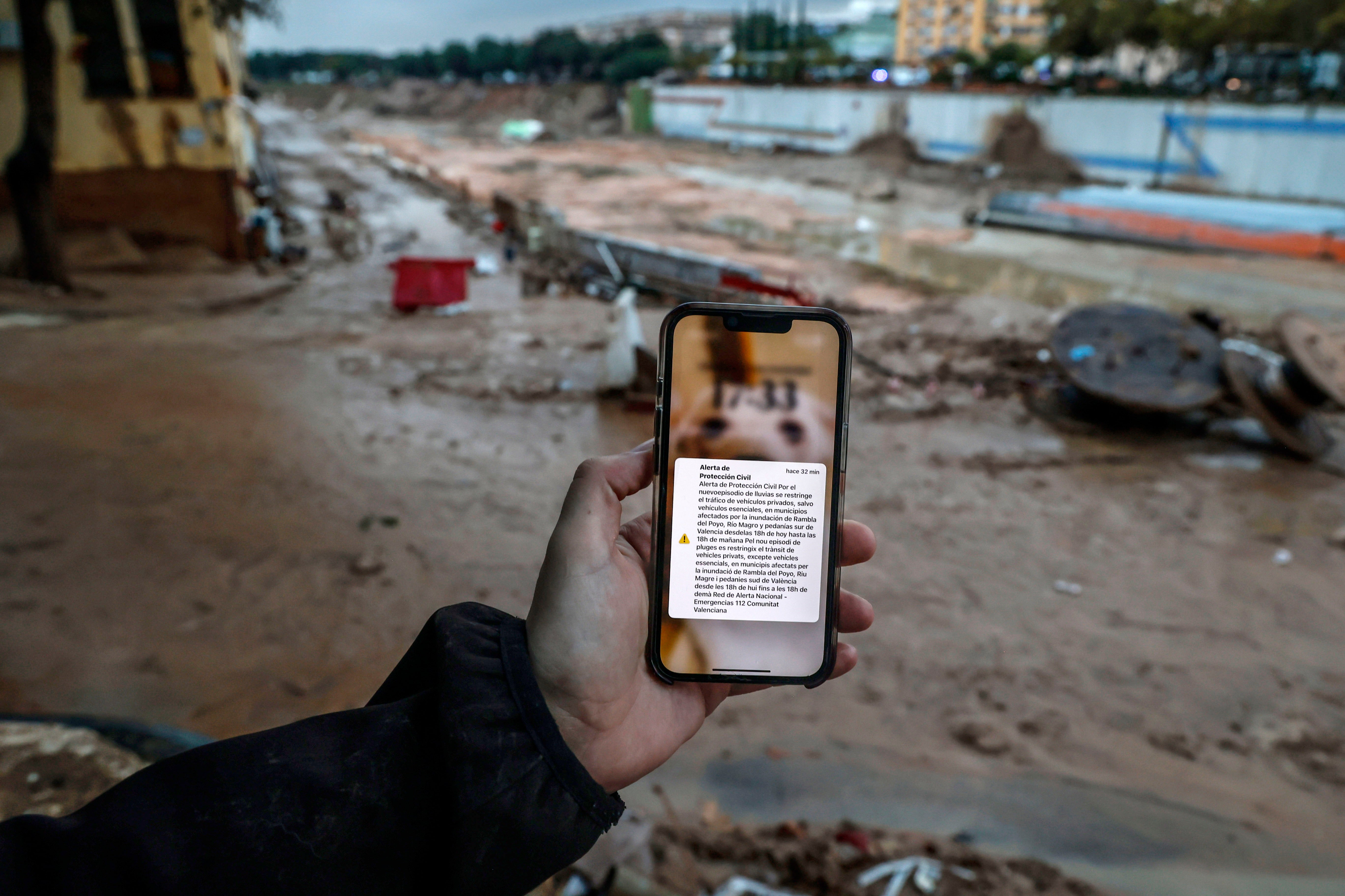 Un hombre sostiene un móvil en medio de una Catarroja embarrada con el Es-Alert que mandó Emergencias a las 20.11 horas del 29 de octubre de 2024.