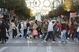 Viandantes con sus compras por un paso de peatones de Valencia en este Black Friday.