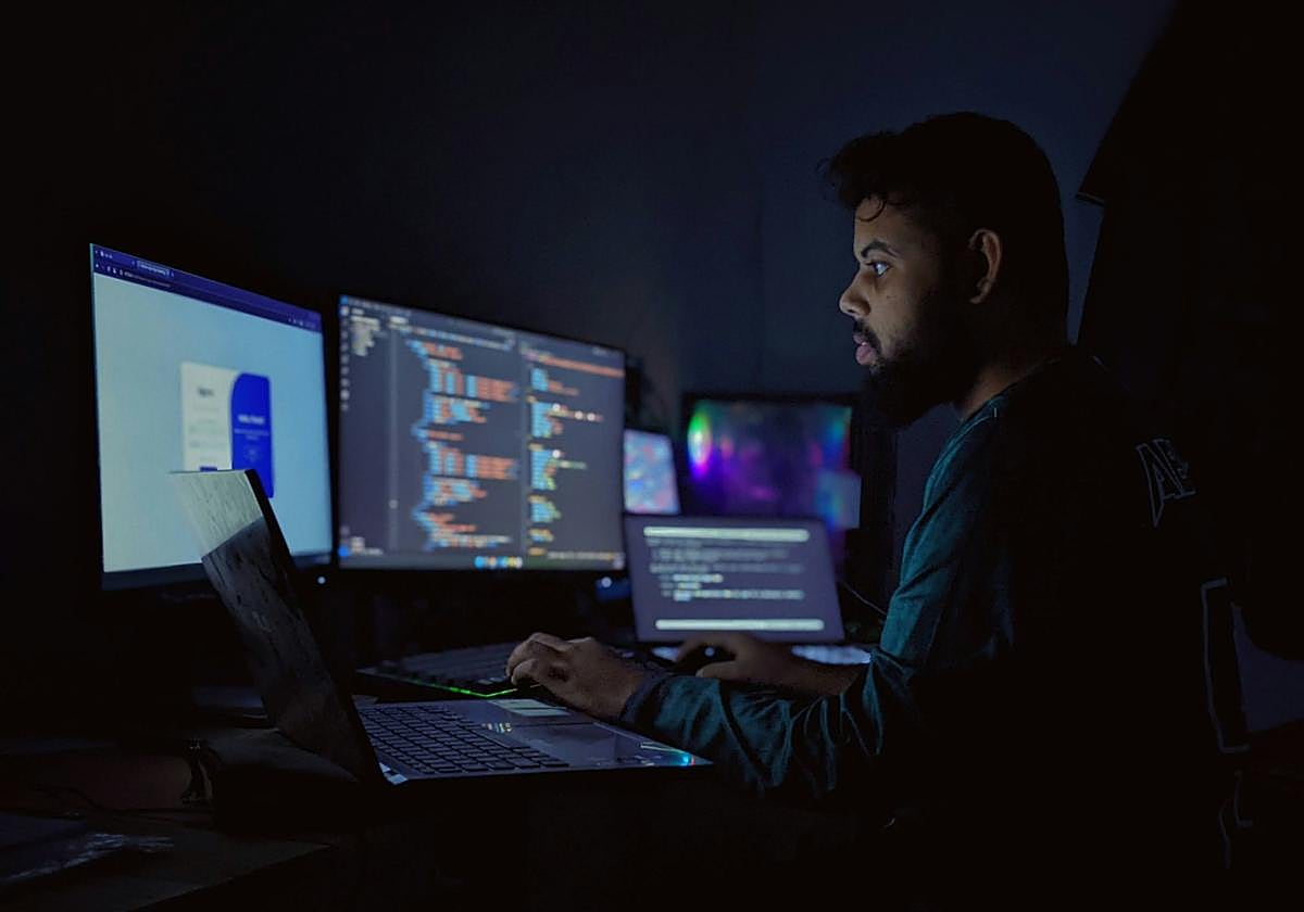 Un hombre trabaja frente a varios ordenadores durante la noche.