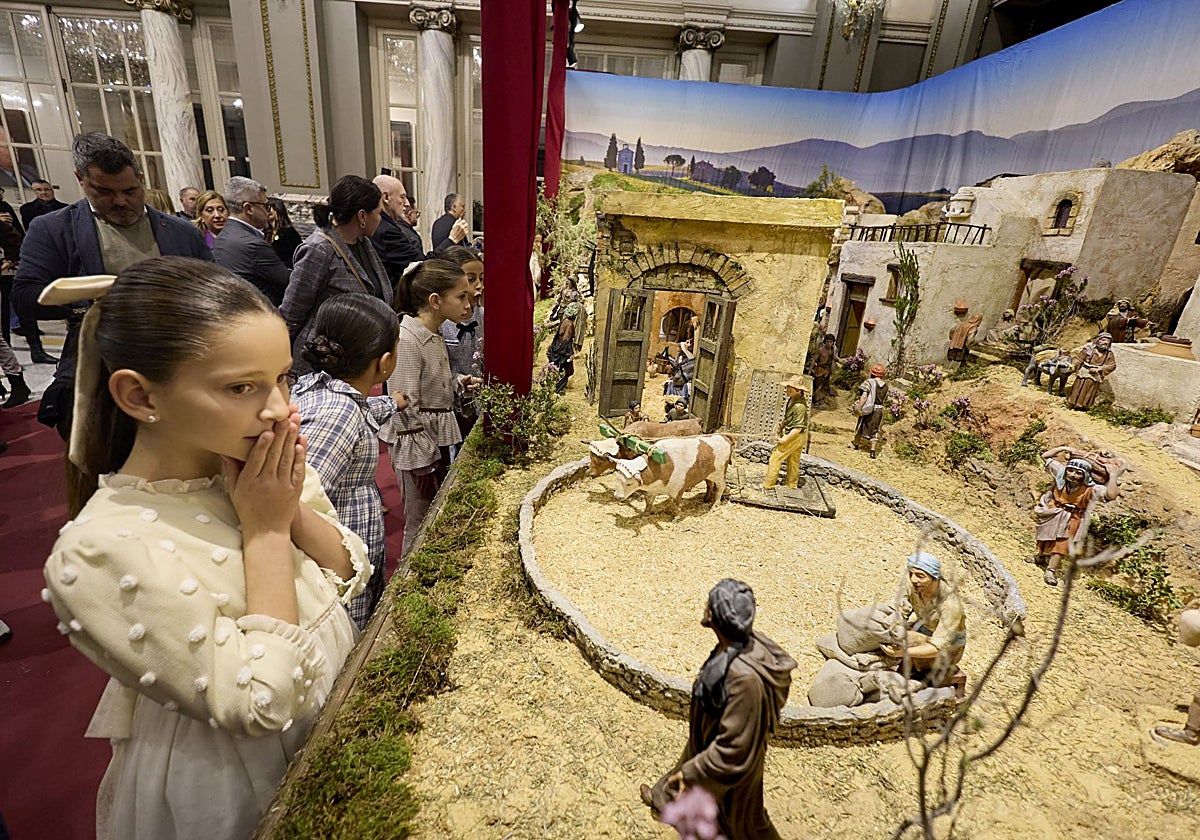 Marta Mercader, fallera mayor infantil de Valencia, y su corte de honor contemplan el belén del Salón de Cristal.