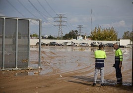 Dos trabajadores vigilan un solar con coches siniestrados por la dana.