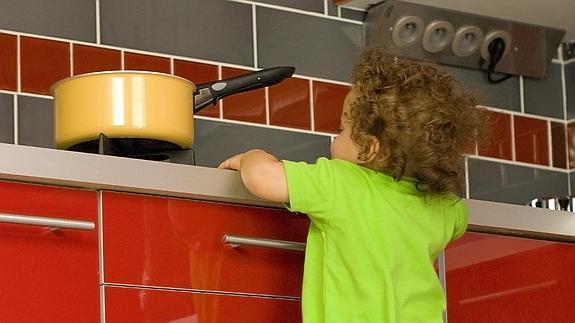 Un niño subido a una silla para alcanzar un cazo en la cocina. 