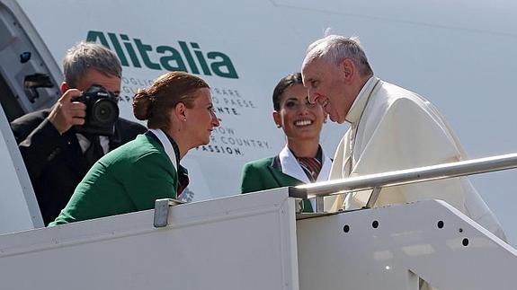 El papa Francisco (d) es recibido por dos azafatas mientras embarca en su avión 