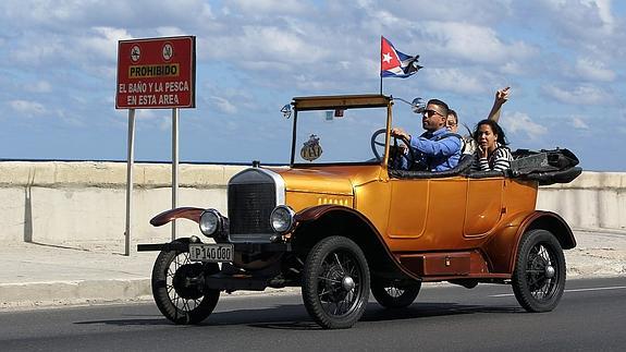 Tres personas viajan en un viejo auto por el malecón. 