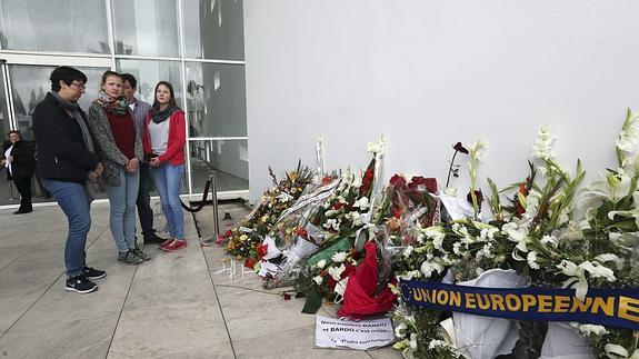 Un grupo de turistas observan los ramos en memoria de las víctimas.