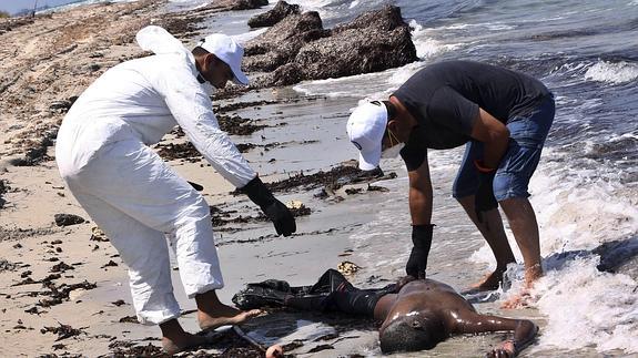 Miembros de la Media Luna Roja comprueban el estado del cuerpo sin vida de un inmigrante en la costa de Libia.