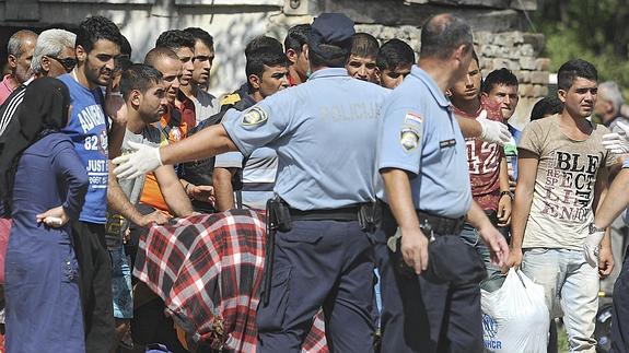 Policías croatas dirigen a varios refugiados a un autobús que les trasladará a un centro de acogida.