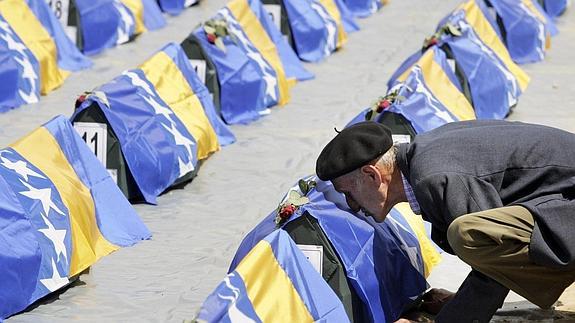 Un anciano besa un féretro cubierto por la bandera bosnia.